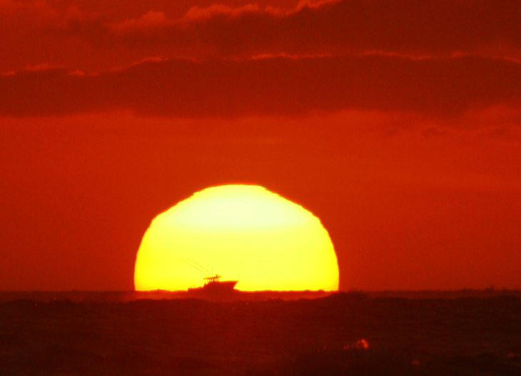 fishing boat silhouetted against rising sun