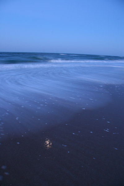 longish exposure, moon reflected in wet sand with surf rolling out