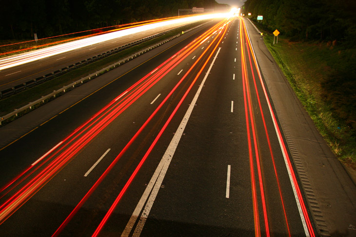 long night exposure from overpass showing light trails and shadow of waving photographer