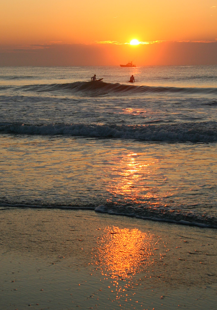 lame surfers and fishing charter against sunrise, Wrightsville Beach NC