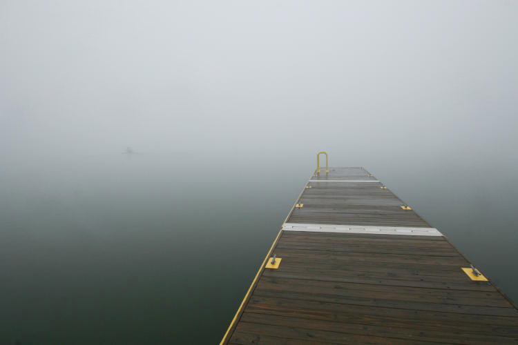 fishing boat disappearing into foggy lake