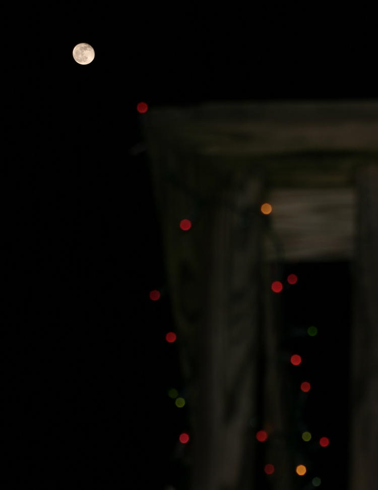 almost full moon along holiday lights on railing