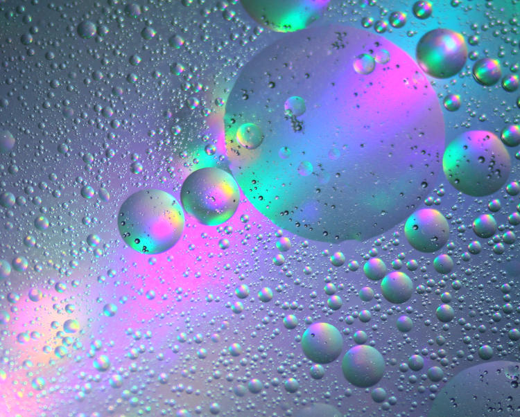 vegetable oil drops in water in a shallow glass pan, backlit by illuminated CD