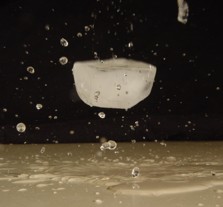 ice cube frozen in mid-air after bouncing in water puddle