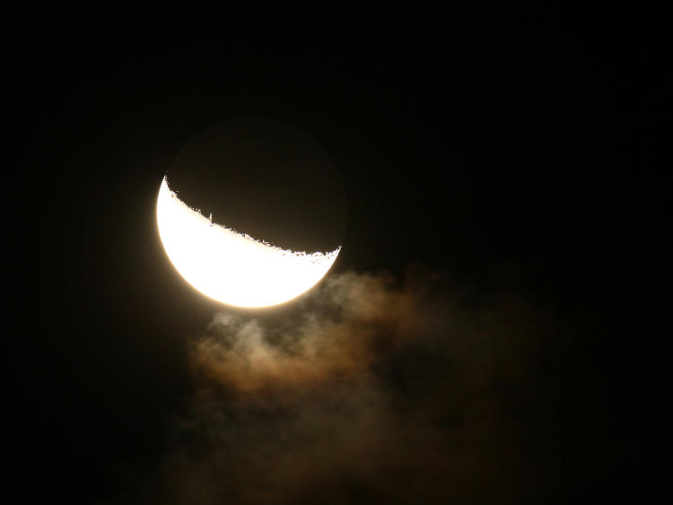overexposed waning crescent moon showing earthshine and passing clouds