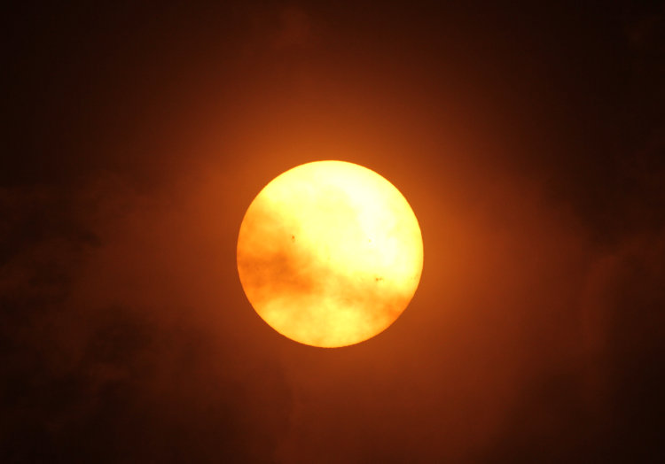 sun breaking through clouds seen through solar filter, with some sunspots beginning to be visible