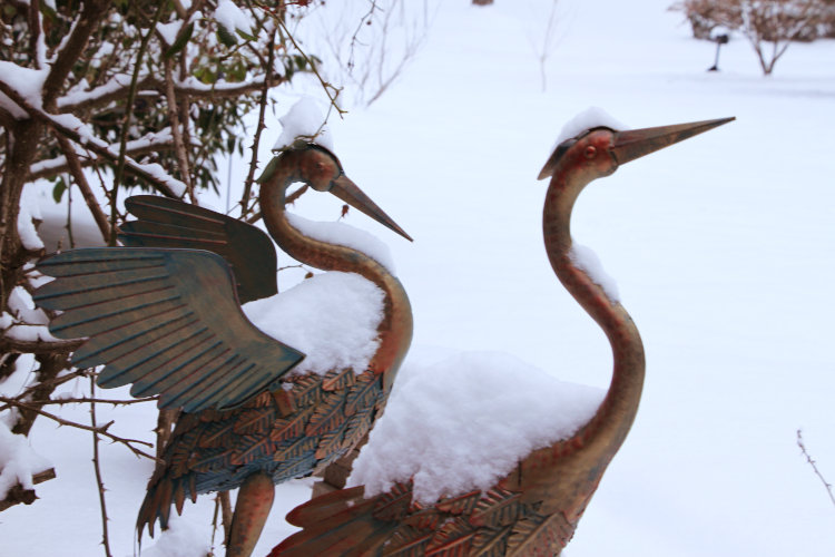 snow piled on decorative bronze-like herons outside Stately Walkabout Manor