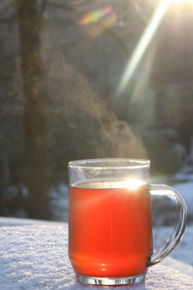 backlit hot mug of tea steaming on snow-covered surface