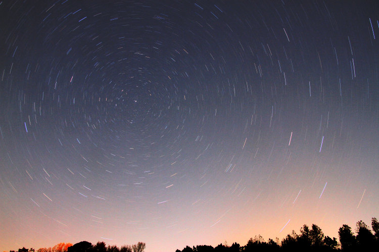 20-minute time exposure of night sky to north showing circular star trails and aurora colors on horizon