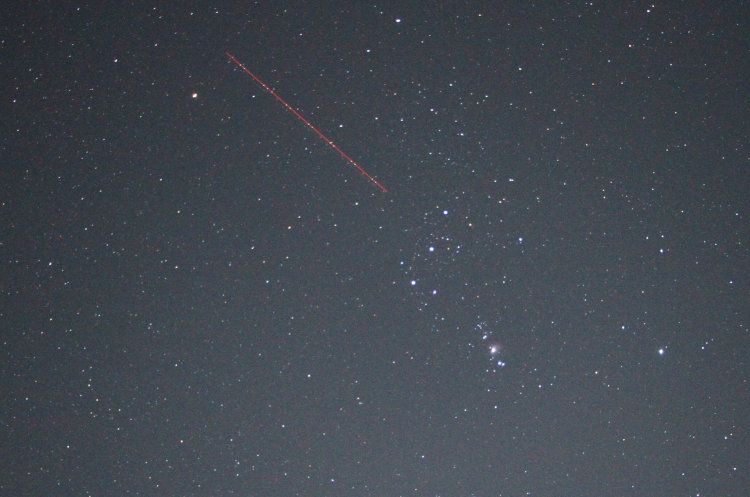night time exposure view of Orion with plane passing through