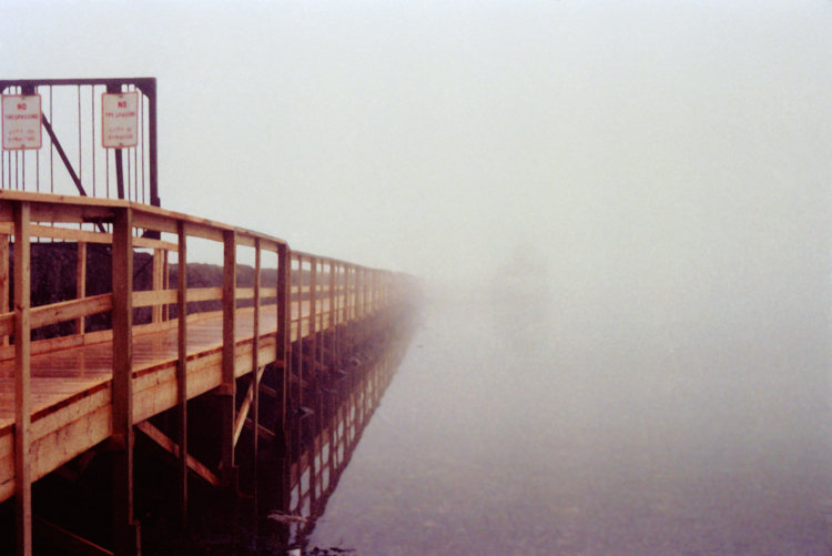 dock on Skaneateles Lake in heavy fog with barest hint of tour boat out there