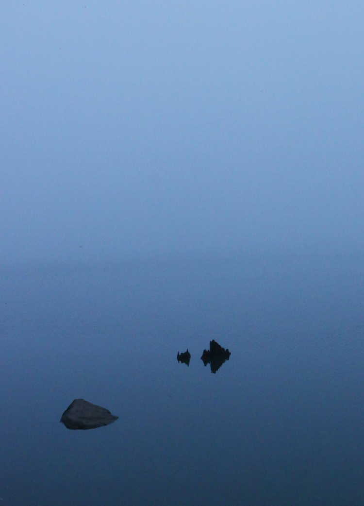 lone rocks protruding from foggy lake surface