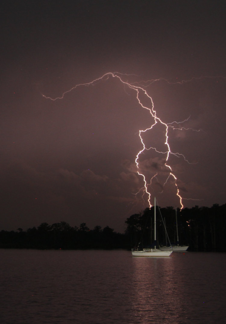 double lightning bolt behind two sailboat masts ob Pamlico River at night