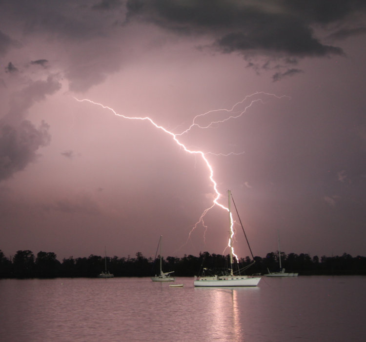 highly visible bolt passing behind sailboat mast on Pamlico River at night