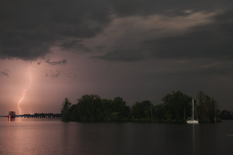 distant semi-obscured lightning alongside small island and sailboat, Pamlico River