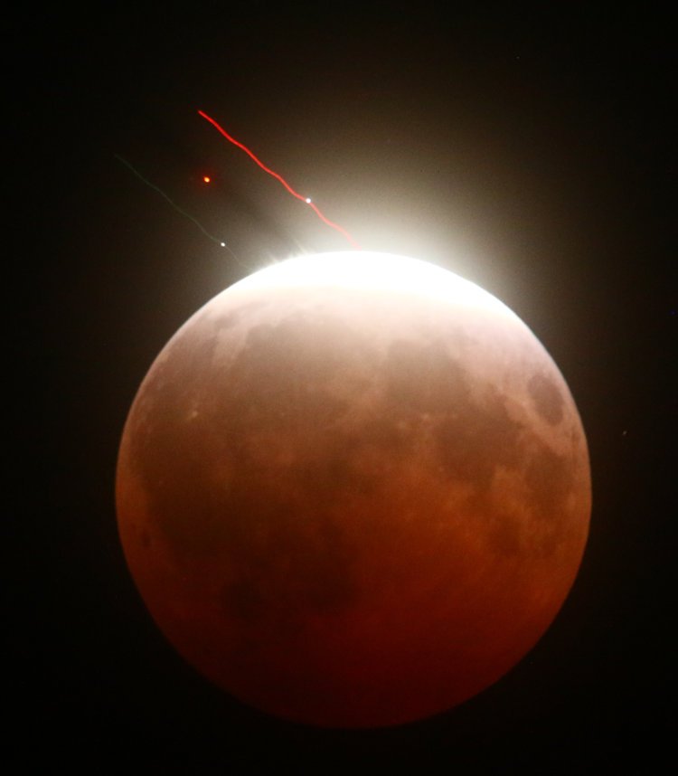 plane crossing in front of partial lunar eclipse of August 27/28, 2026, showing smear on bright edge from contrail and shadow against atmospheric haze