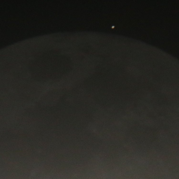 Europa appearing from behind moon delineated by dim earthshine