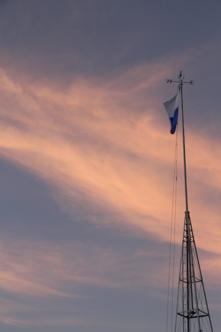 nautical flag on fixed mast and weathervane against twilight colors in sky