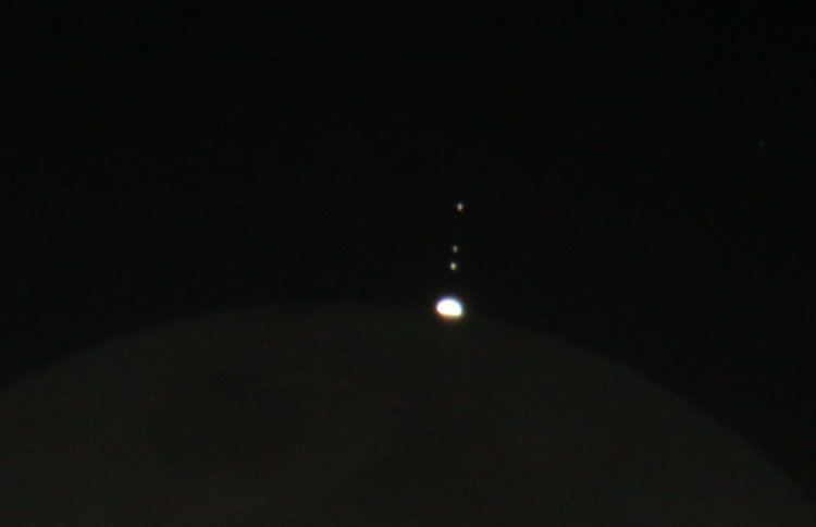 Europa, Callisto, and Io with Jupiter half-emerged from behind moon with earthshine